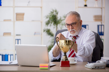 Old male employee being awarded with golden cup
