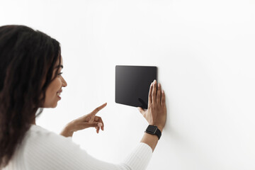 African american woman using digital tablet with blank black screen with smart home control system app, mockup