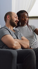 Interracial partners using video call on smartphone in living room. Cheerful multi ethnic couple chatting on online conference via internet for remote communication at home on couch