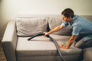 young man using vacuum cleaner on the sofa