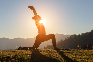Silhouette of woman doing yoga in the mountains at sunset sky background