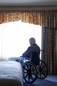 Senior man in wheelchair looking through bedroom window