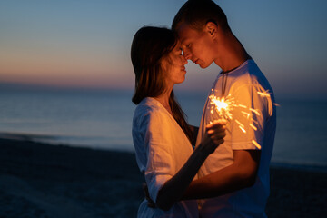 Love on the beach. A loving couple in the evening with sparklers hug each other on a tropical resort. A guy and a girl celebrate Valentine's Day or Christmas on the island.