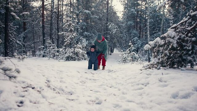 Mother learning her little baby his first steps in the snow forest. High quality 4k footage