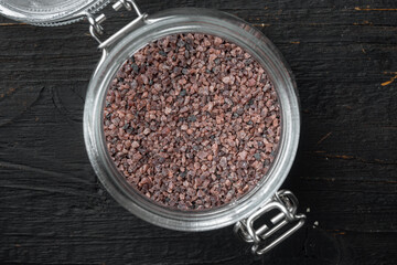 Indian Black salt, Kala namak hindi Healthy food concept, in glass jar, on black wooden background, top view flat lay