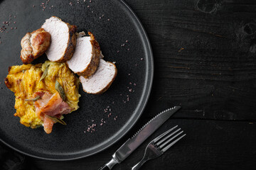 Roasted pork loin with mash potatoe gratin, sage and prosciutto, on plate dish, on black wooden table background , with copyspace  and space for text
