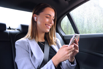 Businesswoman With Wireless Earbuds Commuting To Work In Taxi Talking On Mobile Phone