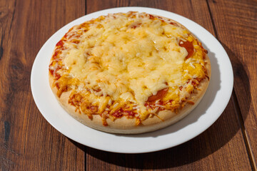 Cooked cheddar cheese pizza on a white plate and dark brown wooden table. Italian style dish. Fast food industry product