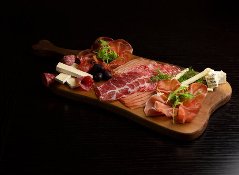 Food tray with delicious salami, pieces of sliced prosciutto, bacon sausage and herbs. Meat platter with selection.
