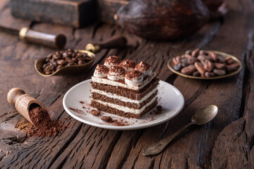 Slice of chocolate cake with tiramisu cream and cocoa powder on wooden table.