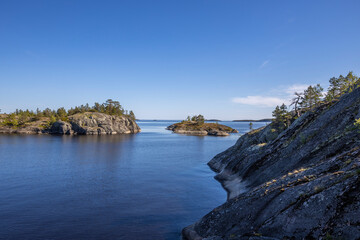 Landscape with a forest on stones over the lake. Sunny day at the lake. Reflection of the sky in the water. Pines on stones. The nature of the north.