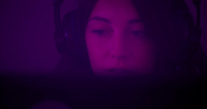 Face portrait of gamer girl playing video games with headphones in neon purple room