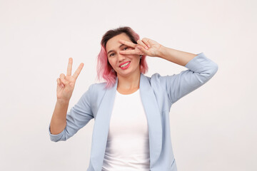 Fototapeta premium Successful businesswoman showing peace, v-sign salute near eye and smiling confident, standing in suit against white background