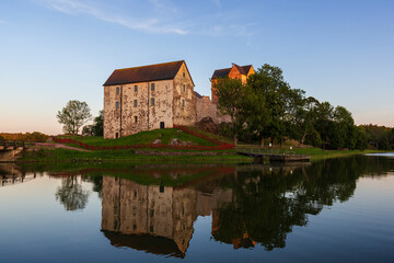 Fototapeta na wymiar Medieval Kastelholm Castle and its reflections on a calm river in Åland Islands, Finland, on a sunny evening in the summer.