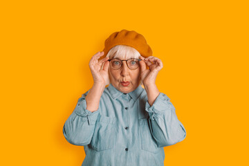 Photo of blonde hair 50s woman astonished face touch glasses look camera isolated over orange color background
