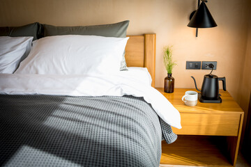 closeup electric kettle and coffee cup on wood night table besides bed