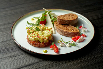 Delicious salmon tartare with avocado and croutons on a plate. wood background. Selective focus