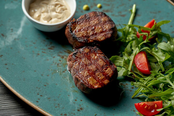 Grilled beef medallions with salad and white sauce.