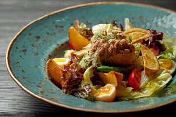 Nicoise salad with tuna and potatoes in a blue plate on a wooden background
