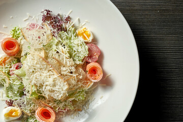 Caesar salad with salmon, parmesan and croutons in a white plate on a dark background