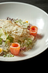 Caesar salad with salmon, parmesan and croutons in a white plate on a dark background
