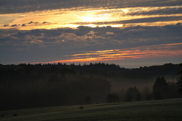 Rising sun on foggy meadow in the morning in Saarland. The sky seems to burn