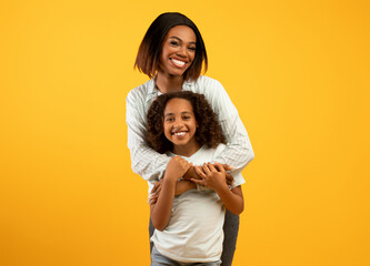 Mother's love. Happy loving african american mom cuddling her daughter from the back, standing over...