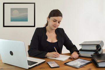 Beautiful Hispanic female executive office worker smiling happy, working sitting at her desk, busy writing in her notebook