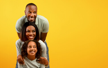 Positive african american family of three looking aside at empty space on yellow background,...