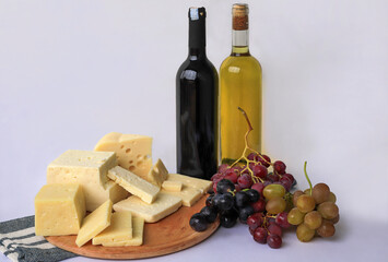 Various types of cheese on a wooden board. White wine , red wine and grapes on a white background.