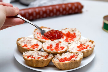 Near the baskets with pate and red caviar, a hand with a spoon of red game.
