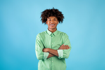 Portrait of african american teen guy with folded arms looking and smiling at camera, posing over...