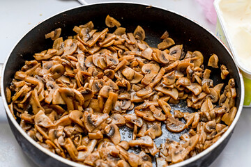 Fried mushrooms, cut into slices, lie in a frying pan on the stove.
