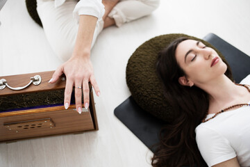 Detail of a woman playing an Indian shruti box in a sound bath session. A woman is seen lying down with her eyes closed.