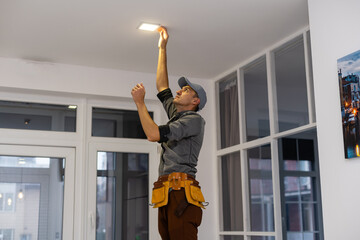 Worker installing lamp on stretch ceiling indoors. Space for text