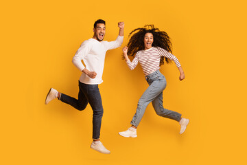 Fototapeta na wymiar Excited Overjoyed Arab Couple Jumping In Air Over Yellow Background