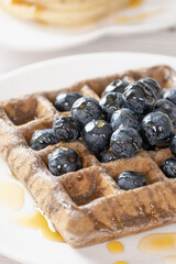 Belgian waffles with fruits berries and honey maple syrup set on white cafe table.