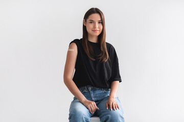 Covid vaccination. Young lady with adhesive plaster on her arm after coronavirus immunization over light background