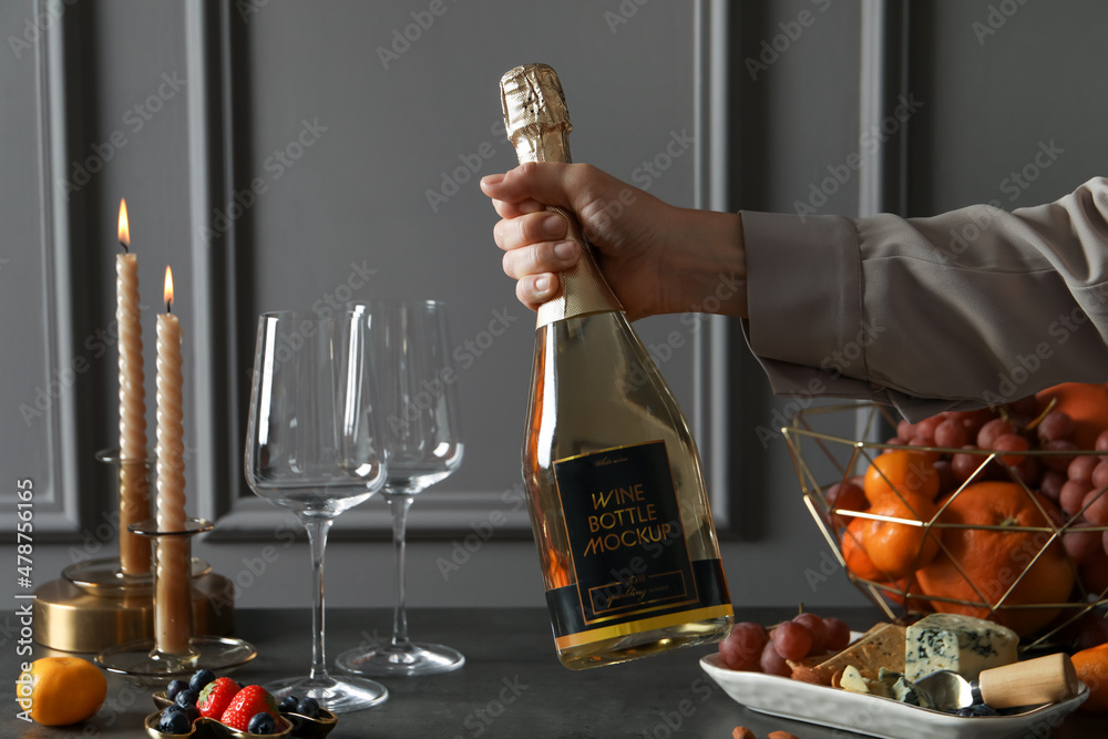 Sticker Woman holding bottle of sparkling wine over table with different snacks, closeup