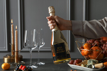 Woman holding bottle of sparkling wine over table with different snacks, closeup