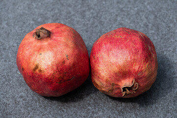 Fototapeta na wymiar Zwei rote Granatäpfel liegen auf einer grauen Steinplatte - Granatapfel (Lat.: Punica granatum)