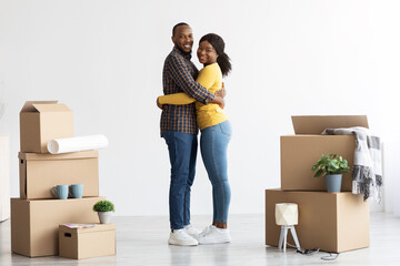 Happy Black Spouses Embracing At New Home Among Cardboard Boxes With Belongings