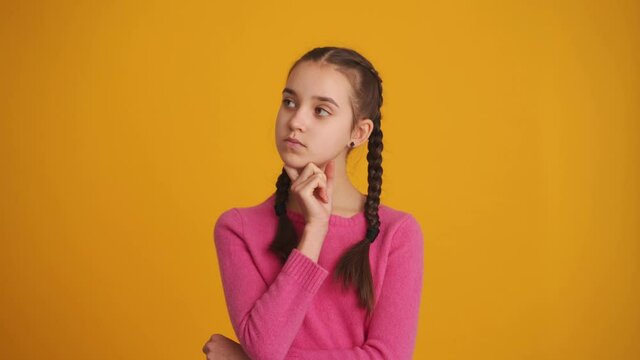 Pensive girl with pigtails looking around in the yellow studio