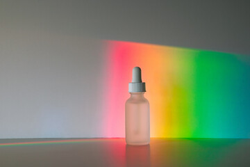 Face serum in matte glass bottle with a dropper in front of vibrant rainbow prism background. Front...