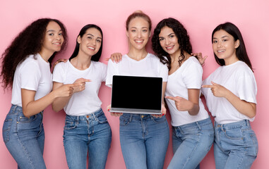 Diverse Women Holding Laptop Pointing At Empty Screen, Pink Background