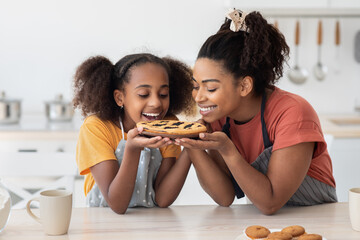 Delighted black mother and teen daughter smelling homemade pie