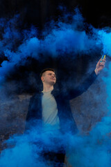 Obraz premium The guy holds in his hands colored smoke of blue on a black background.