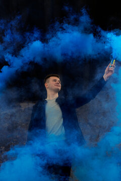 The guy holds in his hands colored smoke of blue on a black background. © Юлия Усикова