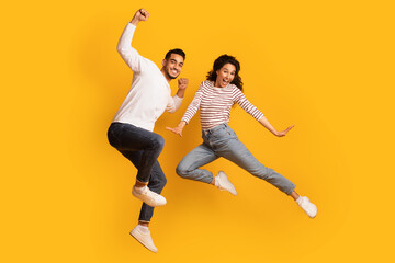 Fototapeta na wymiar Crazy Fun. Joyful Excited Middle-Eastern Couple Jumping In Air Over Yellow Background