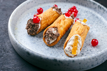 Traditional Italian Sicilian pastry dessert cannoli with creamy ricotta filling, chocolate crisps and fresh currant fruit served as close-up on a Nordic design plate - obrazy, fototapety, plakaty